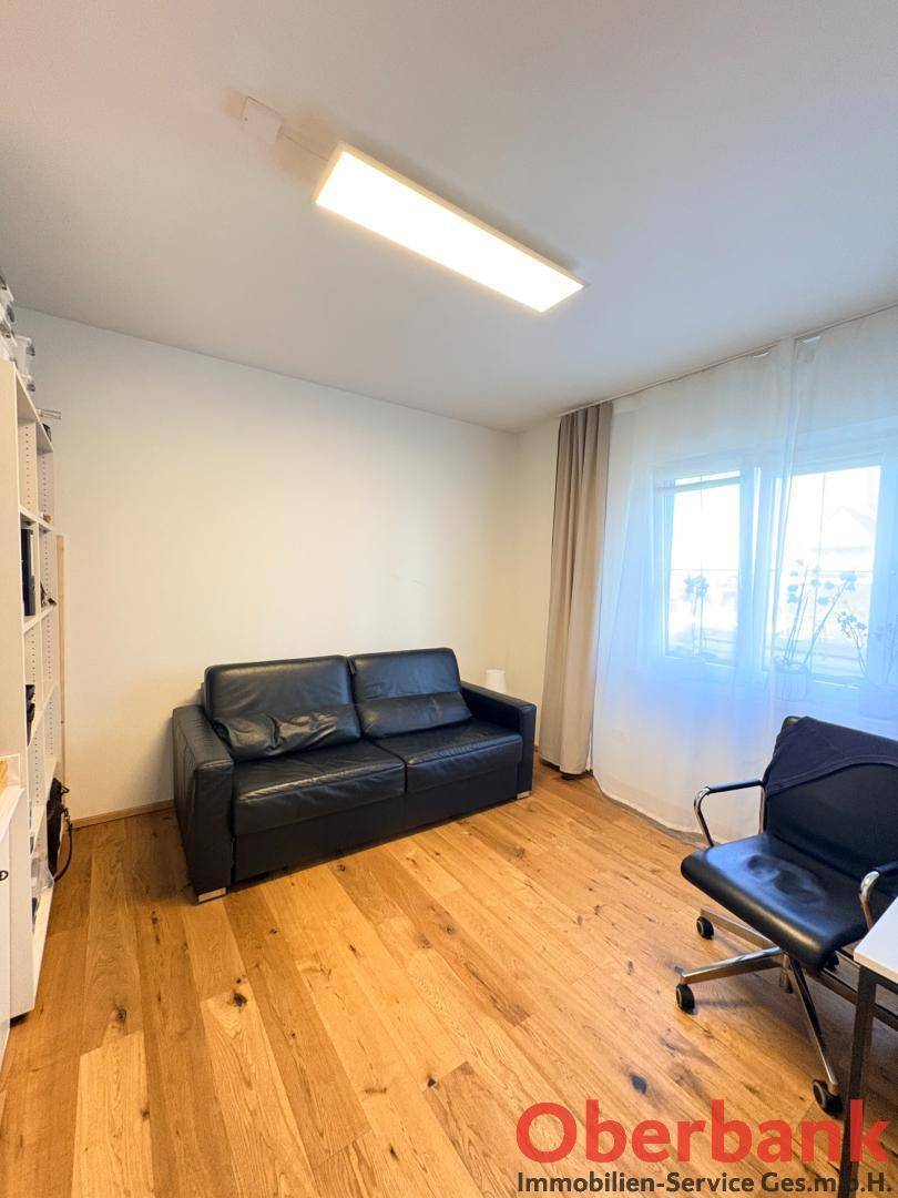 Funktionales Arbeitszimmer mit schwarzem Sofa, Schreibtischstuhl und hellem Holzboden.