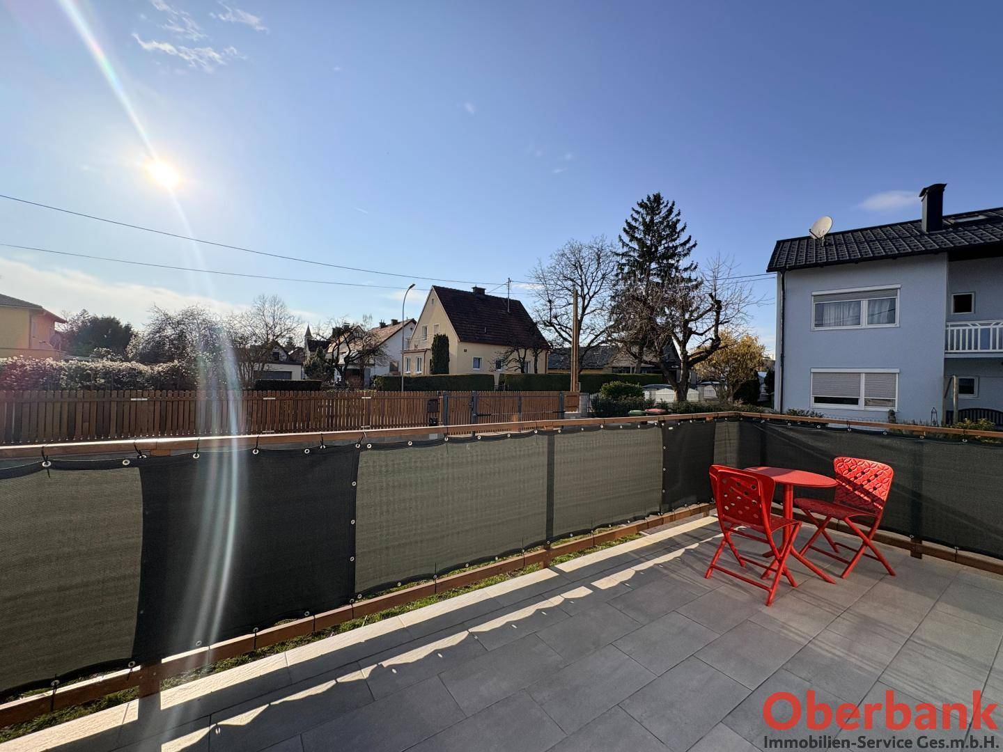Sonniger Balkon mit roter Sitzgruppe und weitem Blick über die umliegende Wohngegend.