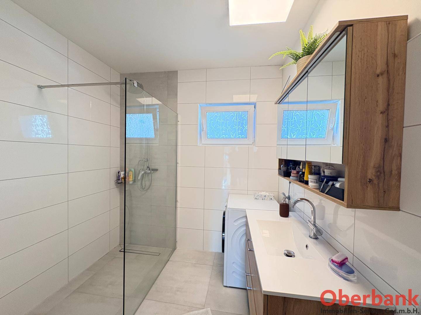 Modernes Badezimmer mit weißen Fliesen, ebenerdiger Dusche und Waschbecken mit Unterschrank.