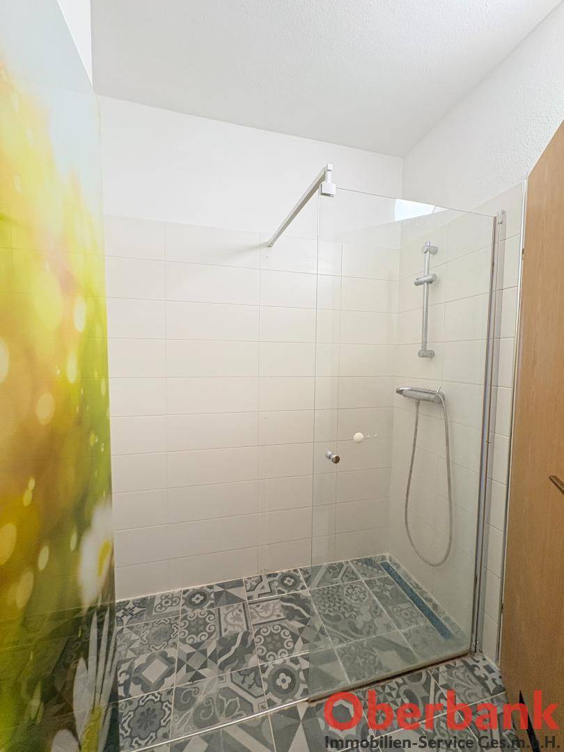 Badezimmer mit begehbarer Dusche und modernen Fliesen, die ein frisches Ambiente schaffen.