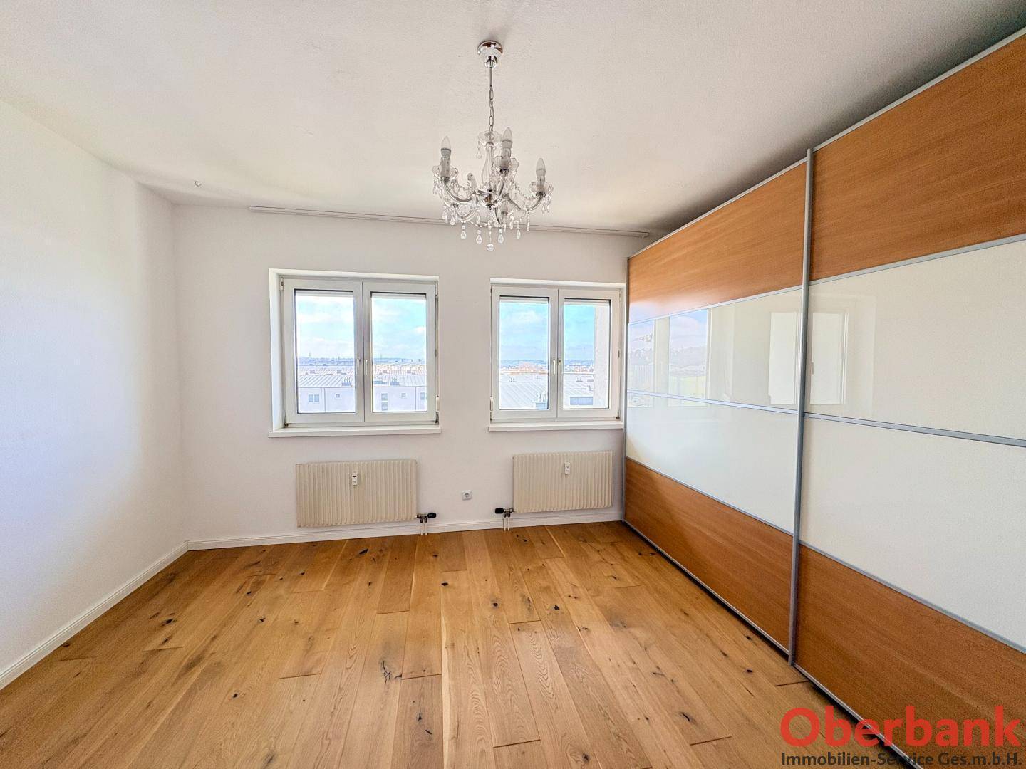 Schlafzimmer mit Holzboden, großen Fenstern und einem geräumigen Einbauschrank.