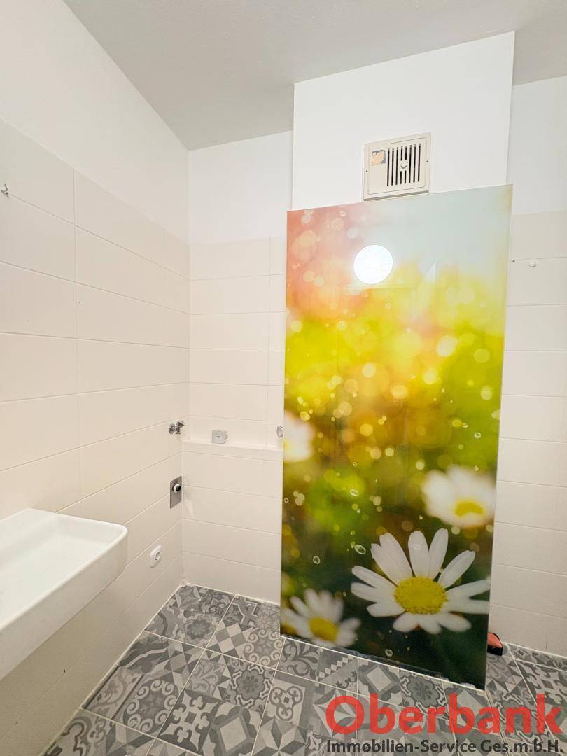 Modernes Badezimmer mit weißen Wandfliesen, gemustertem Boden und dekorativer Duschwand.
