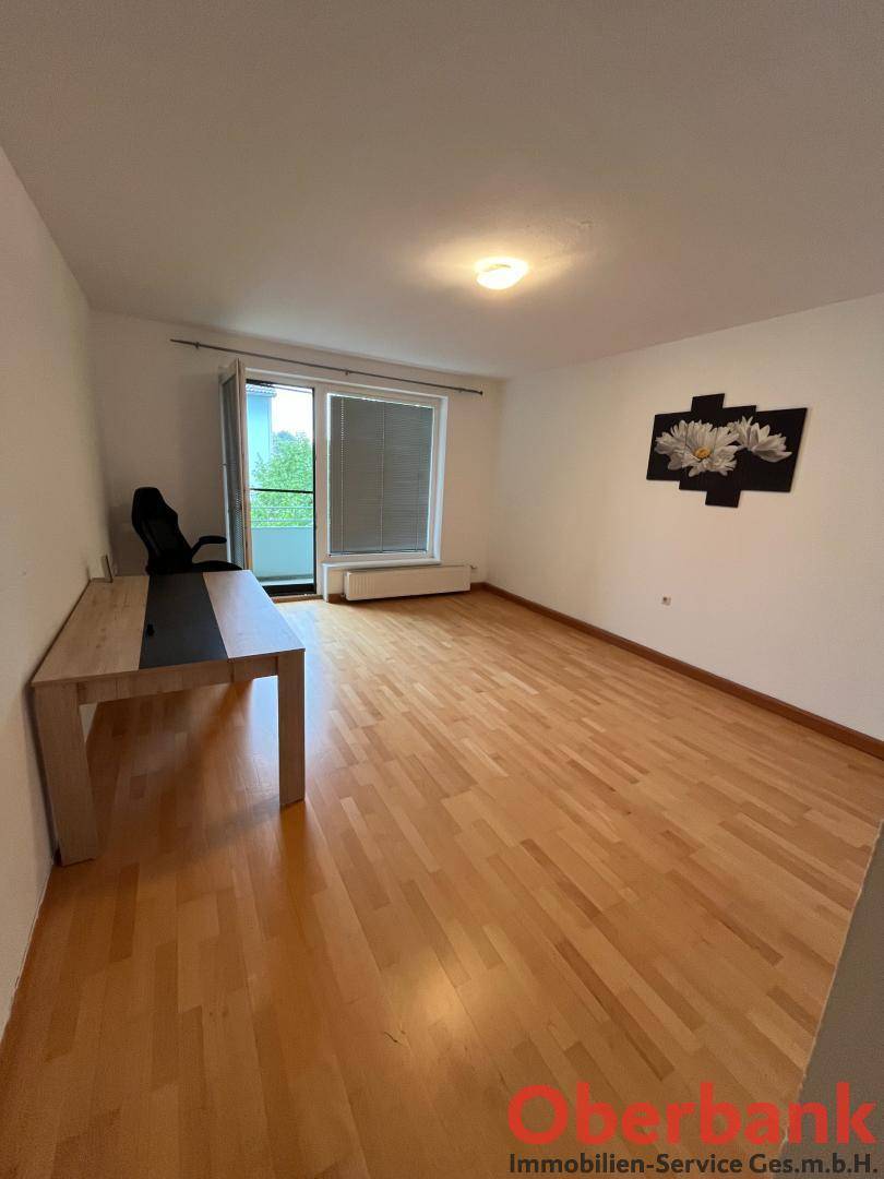 Geräumiges Zimmer mit Holzboden und Zugang zu einem Balkon.
