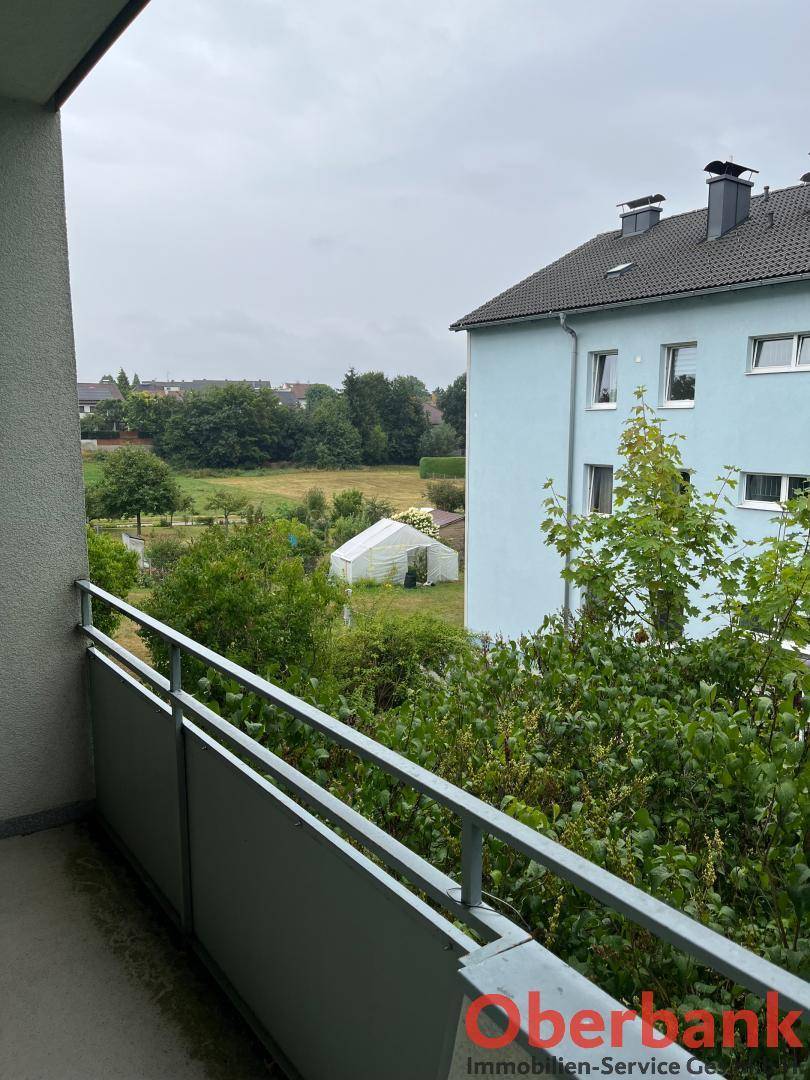 Blick vom Balkon auf einen grünen Gartenbereich und benachbarte Gebäude.