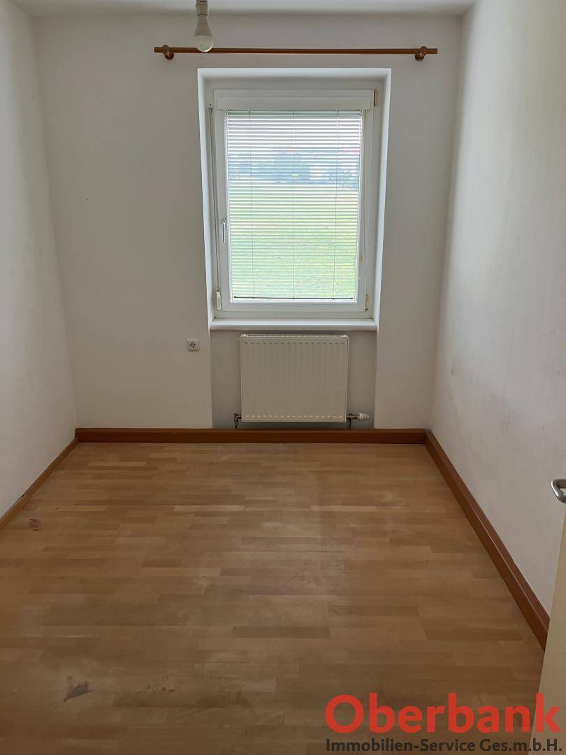 Leeres Zimmer mit Holzboden und Fenster, ideal als Schlaf- oder Arbeitszimmer.