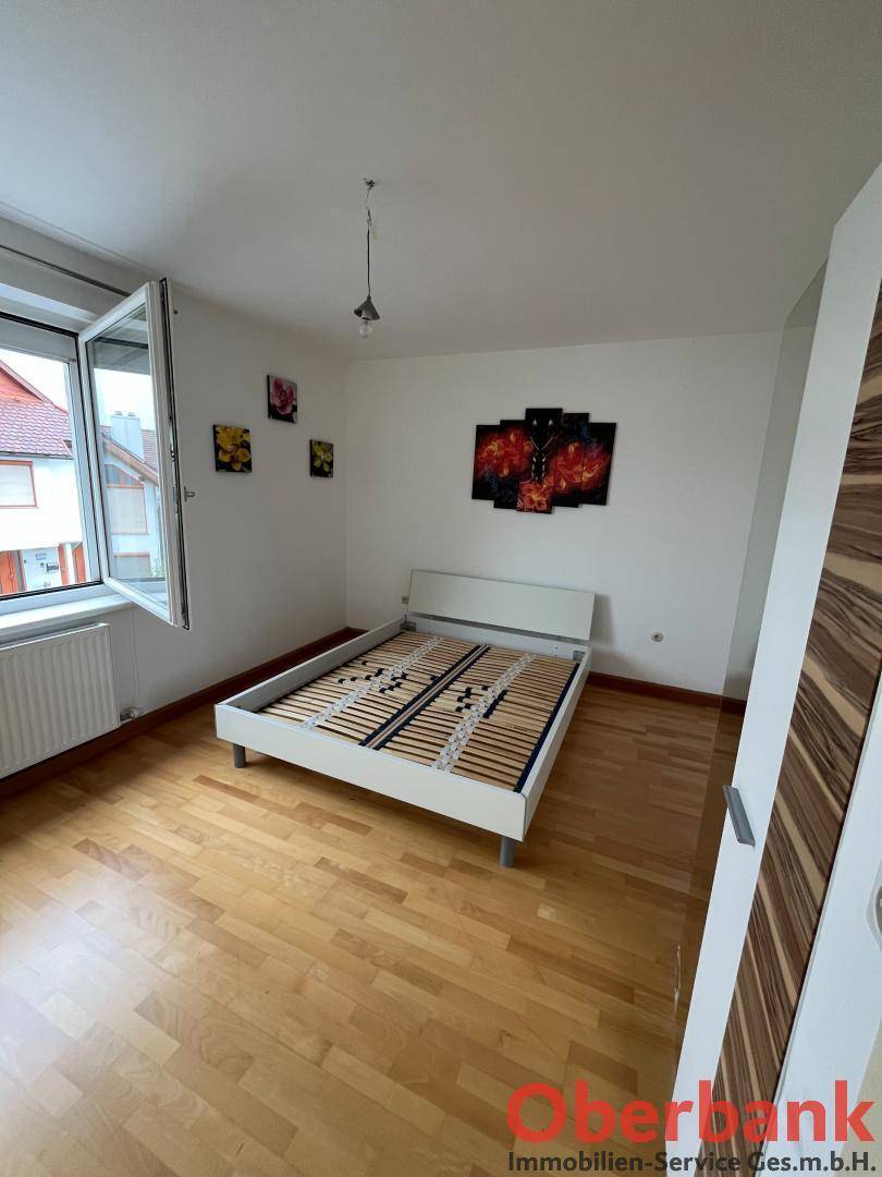 Schlafzimmer mit Holzboden, weißem Bettrahmen und Fenster.