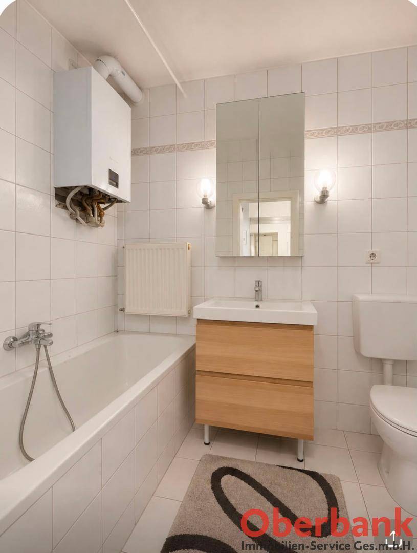 Gefliestes Badezimmer mit Badewanne, WC, Waschbecken und Spiegelschrank.
