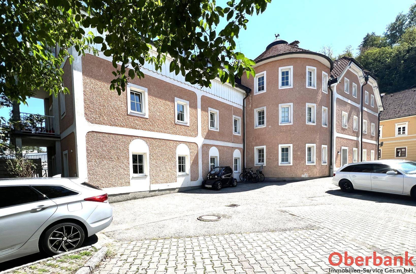 Historisches Gebäude mit runder Fassade und Parkplätzen davor, umgeben von Bäumen.