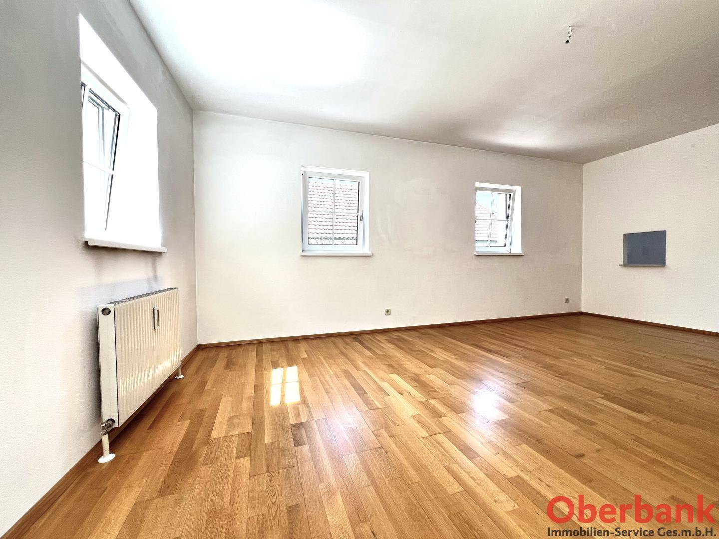 Heller Wohnraum mit Parkettboden, mehreren Fenstern und Heizkörpern, bereit zur Einrichtung.