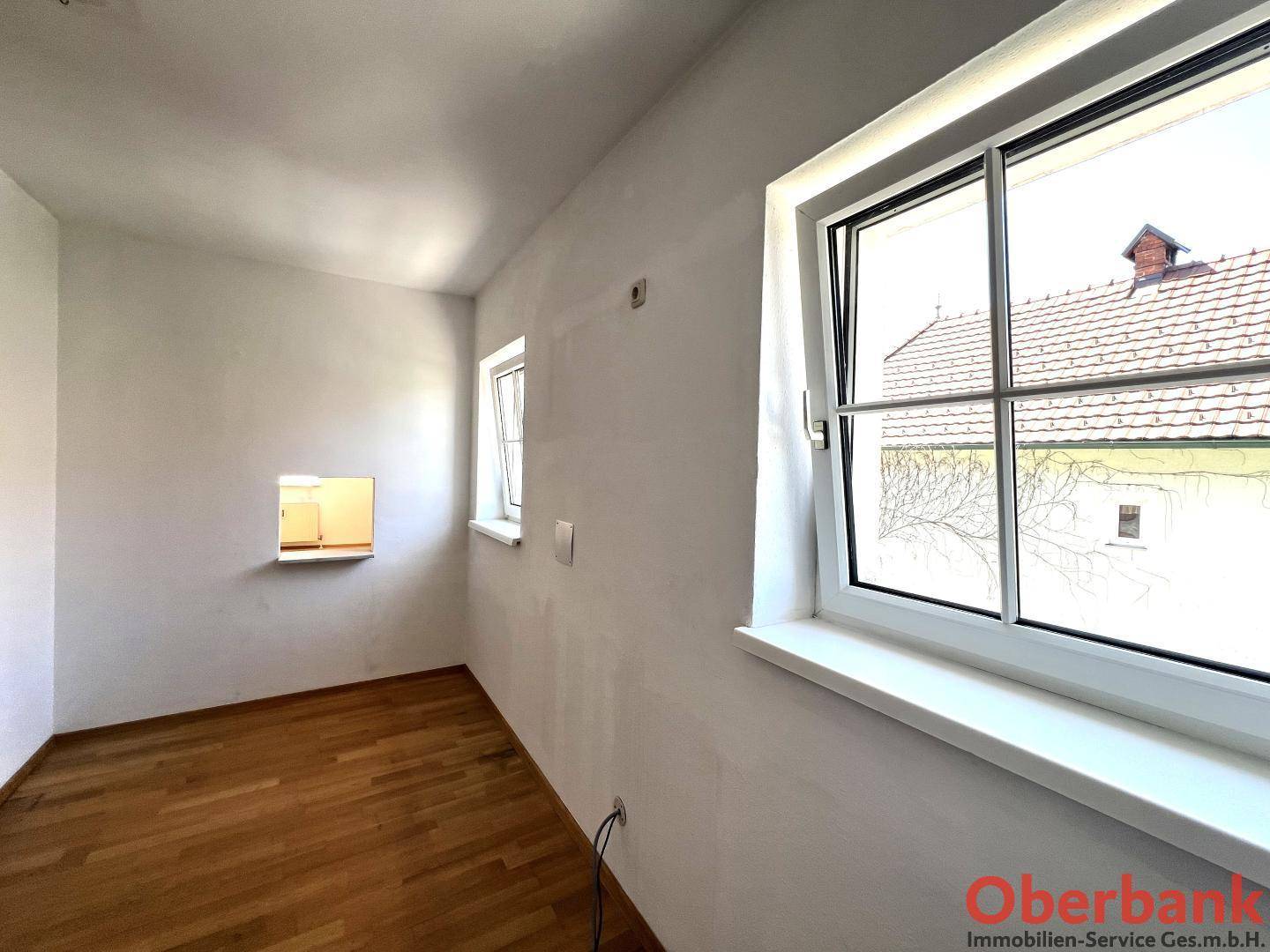 Heller Wohnraum mit Parkettboden und Blick auf die umliegenden Dächer durch das Fenster.