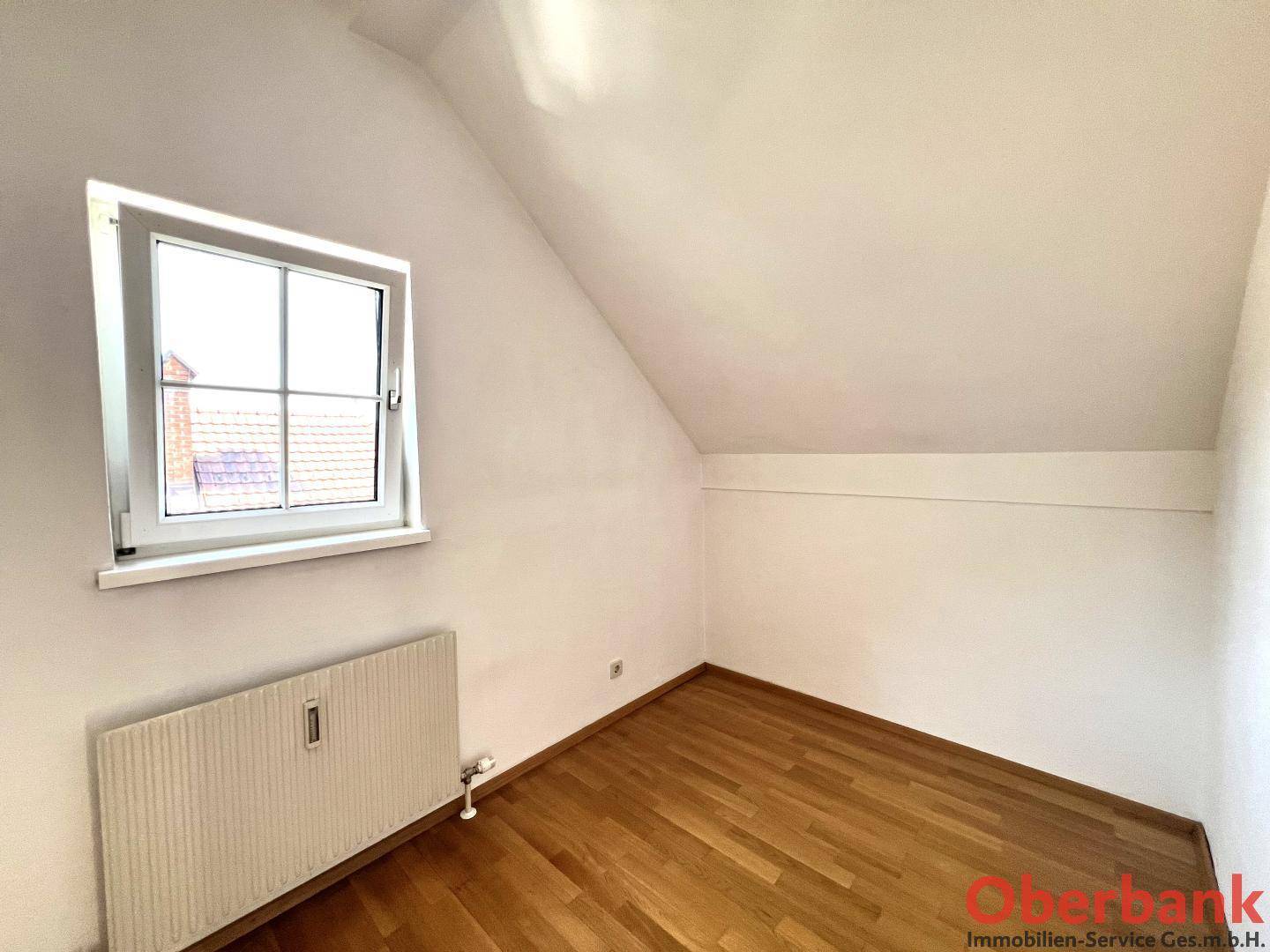 Kleines Dachzimmer mit Holzboden, Dachschräge und einem Fenster, ideal als Schlafzimmer.