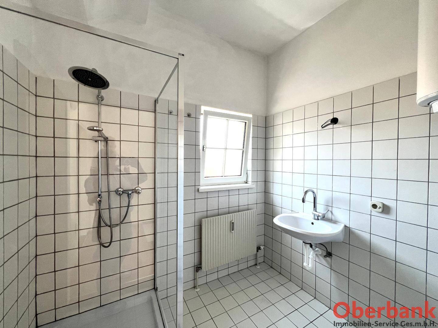 Modernes Badezimmer mit Dusche, Waschbecken und weiß gefliesten Wänden, inklusive Fenster.