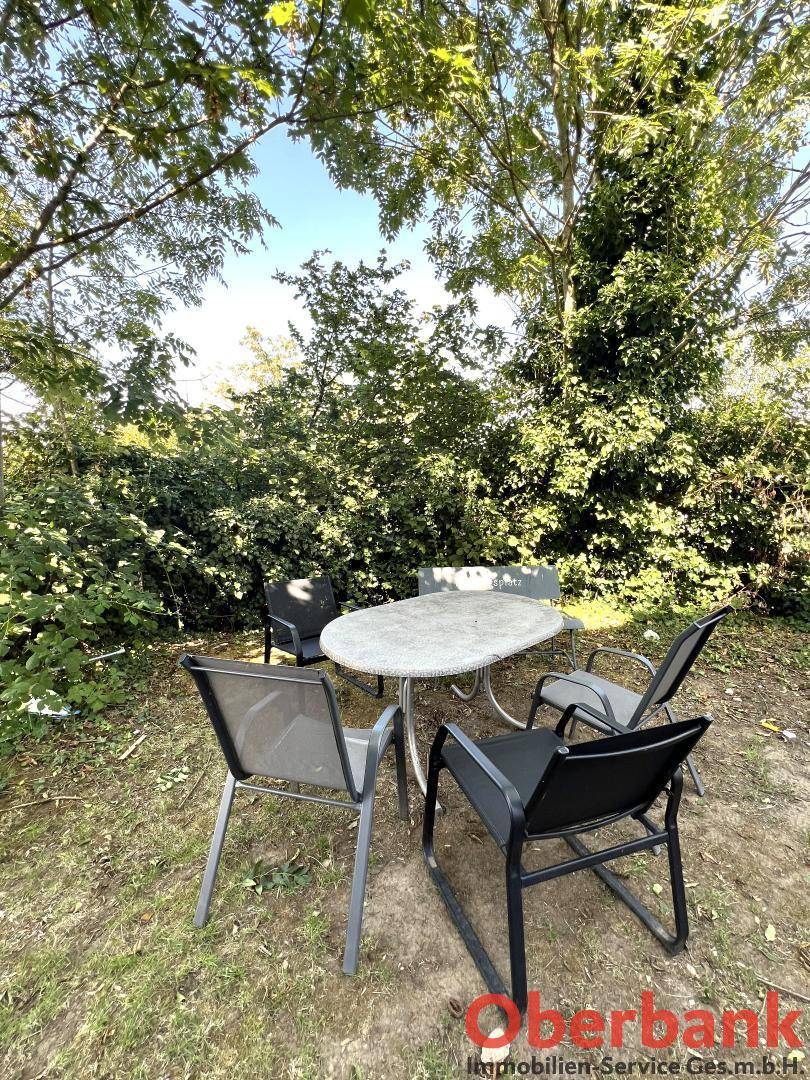 Gemütlicher Sitzbereich im Garten unter Bäumen mit Gartentisch und Stühlen für Entspannung.