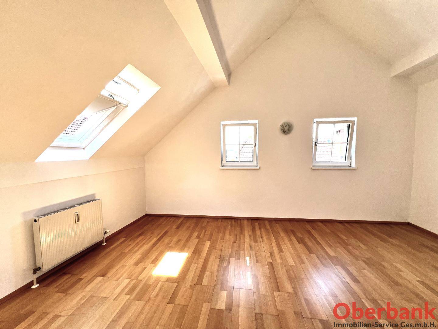 Geräumiges Dachzimmer mit Holzboden, Dachschräge und einem großen Dachfenster.