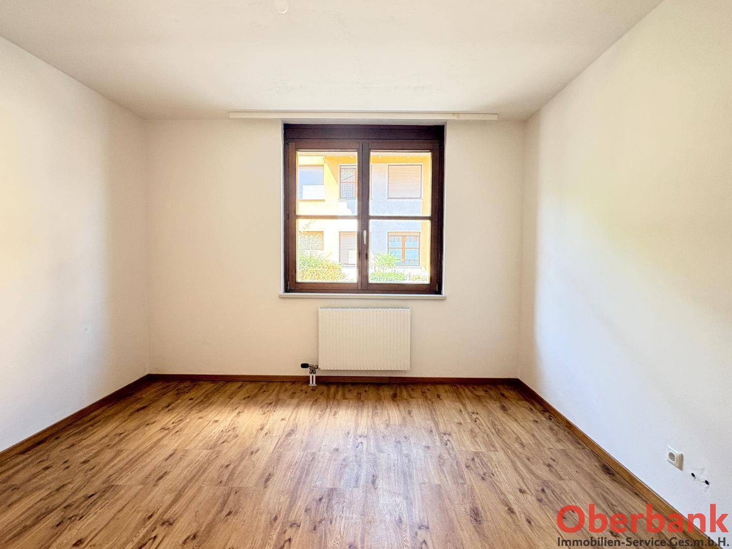 Geräumiges Zimmer mit Laminatboden und einem großen Fenster, das den Raum hell erscheinen lässt.