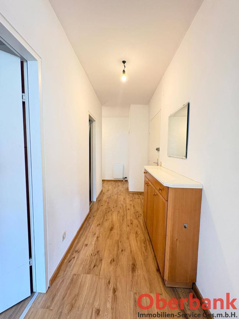 Heller Flur mit Laminatboden und einem kleinen Schrank mit Spiegel.