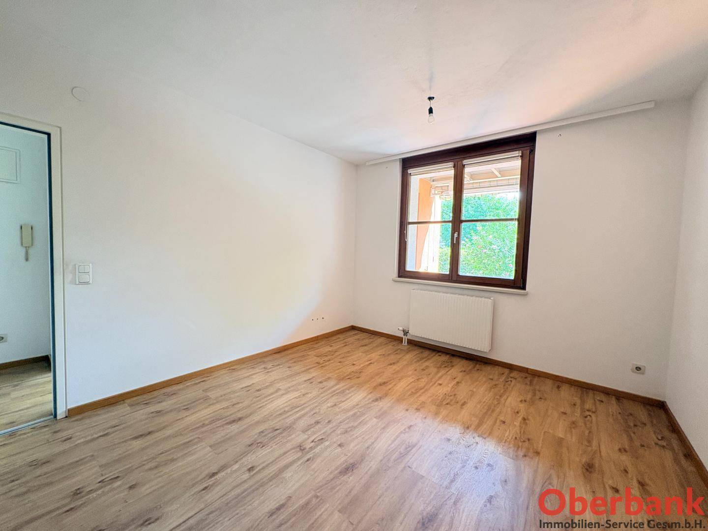 Helles Schlafzimmer mit Laminatboden und einem Fenster, das viel Tageslicht hereinlässt.