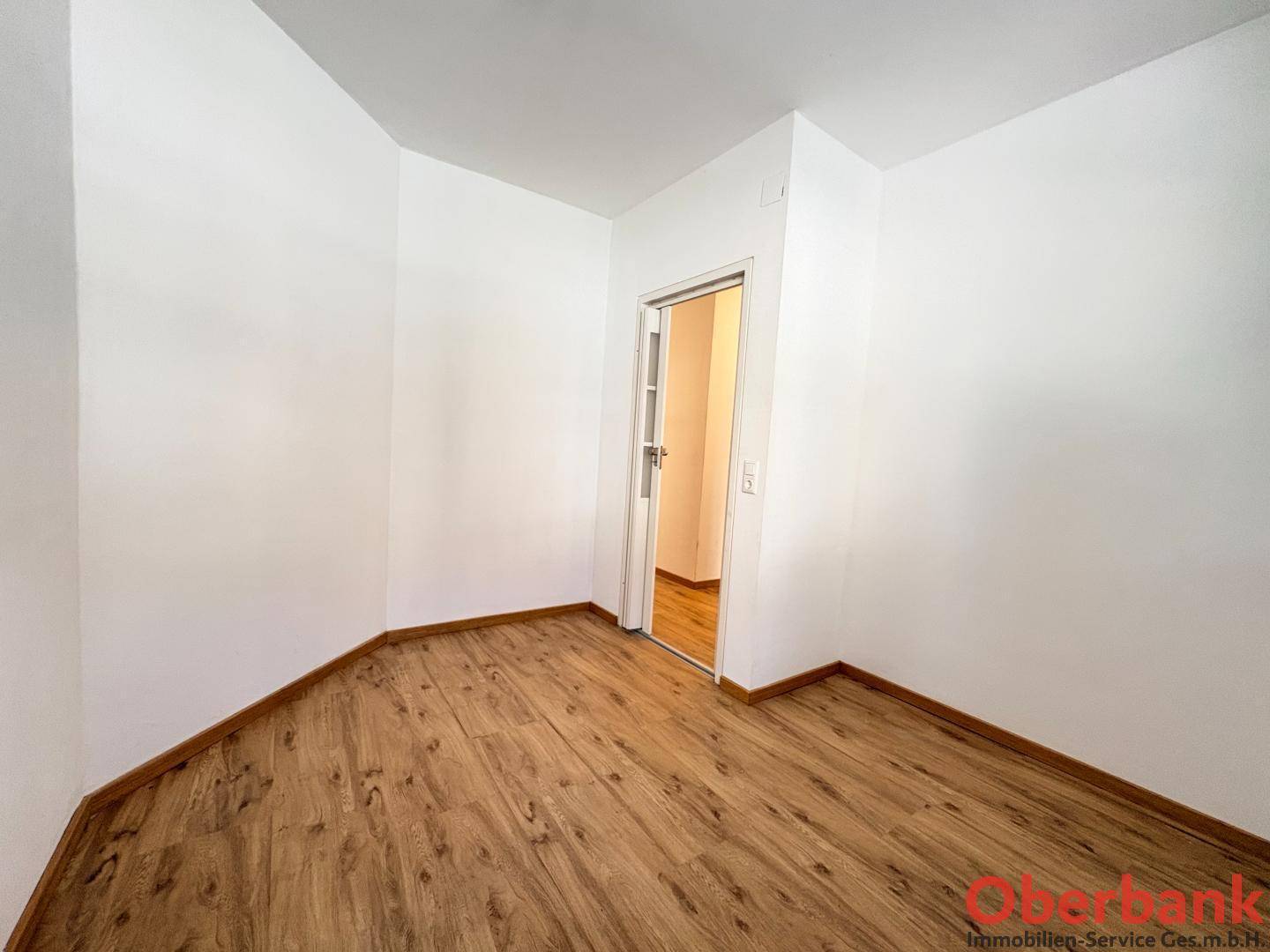 Leeres Zimmer mit Laminatboden und einer Tür, die zu einem weiteren Raum führt.
