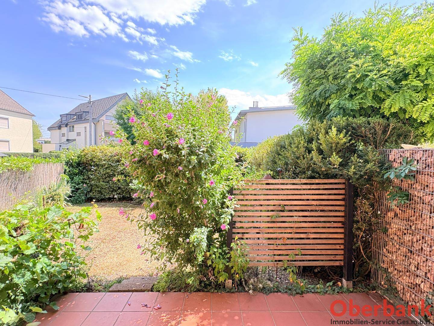 Kleiner, gepflegter Gartenbereich mit Terrasse, umgeben von Sträuchern und einem Holzzaun.