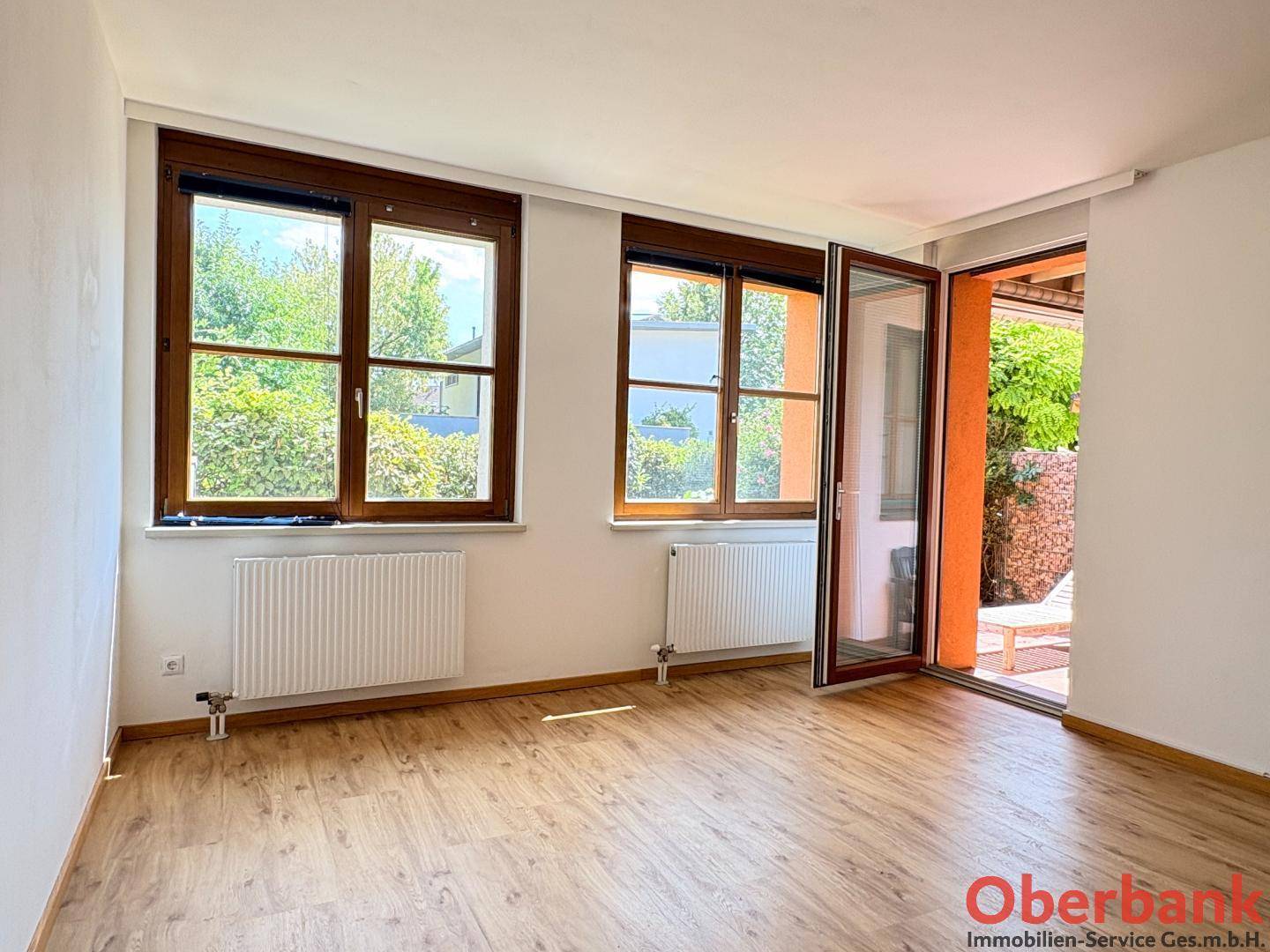 Helles Wohnzimmer mit Laminatboden, großen Fenstern und direktem Zugang zur Terrasse.