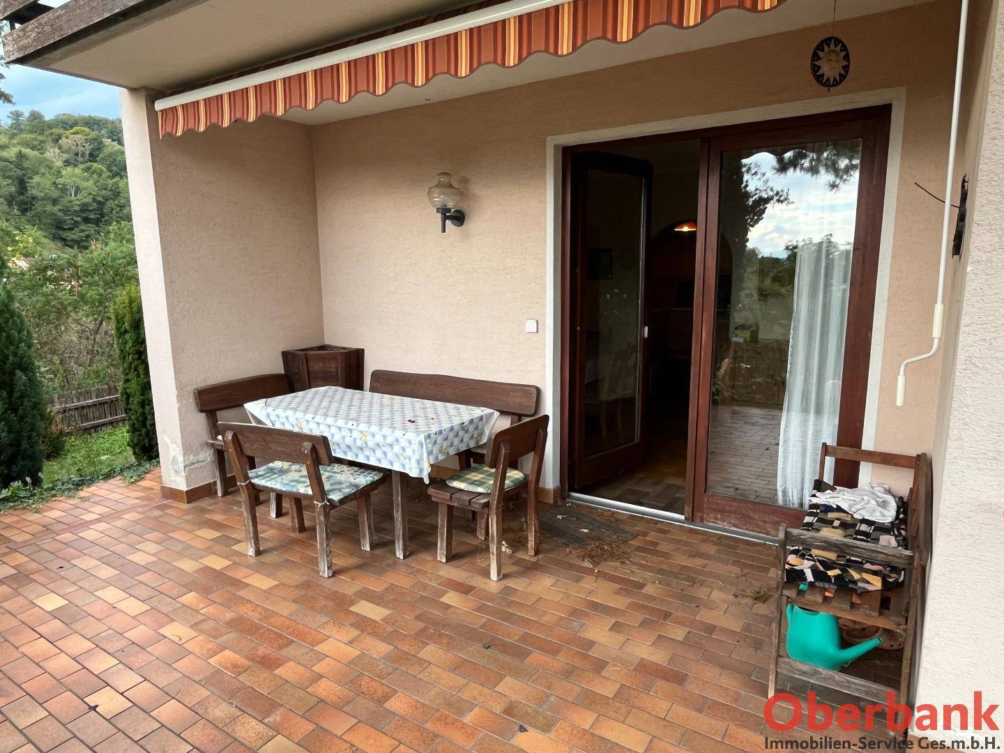 Gemütliche Terrasse mit Fliesenboden, Gartenmöbeln und einer gestreiften Markise für angenehmen Schatten.
