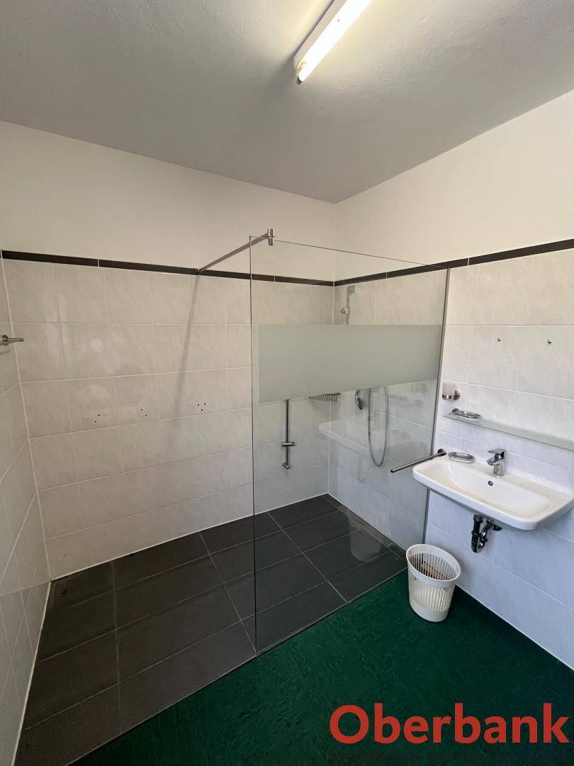 Modernes Badezimmer mit begehbarer Dusche, weißen Fliesen an den Wänden und einem einzelnen Waschbecken.