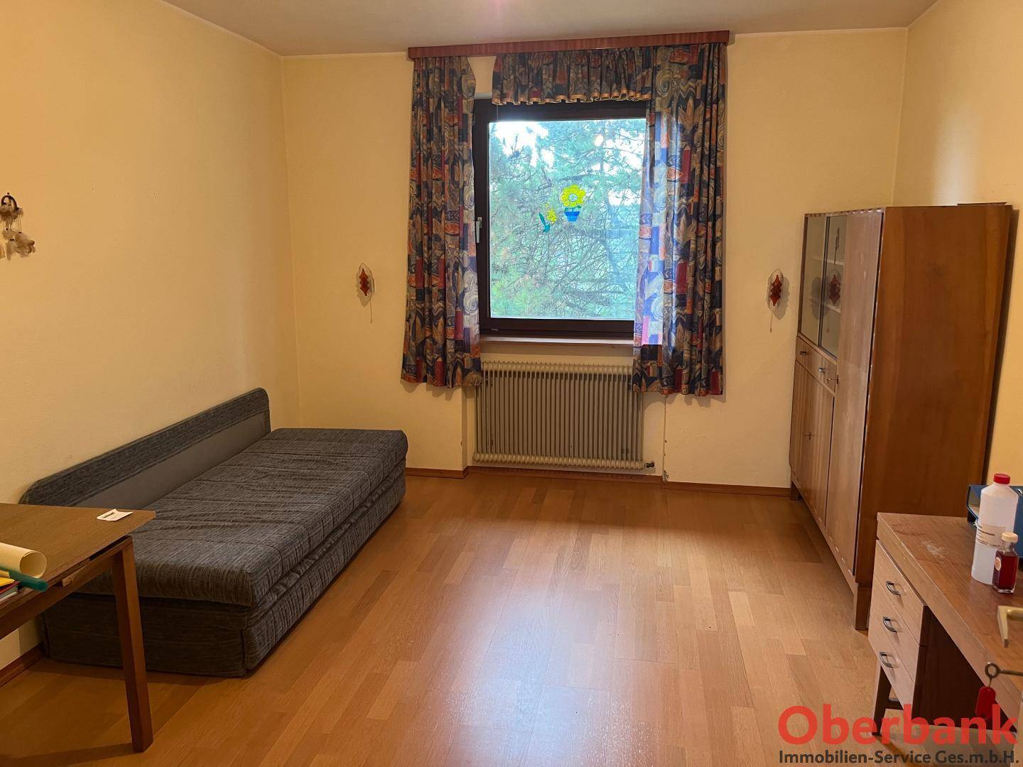 Helles Schlafzimmer mit Holzboden, Einzelbett und einem großen Fenster mit Blick ins Grüne.