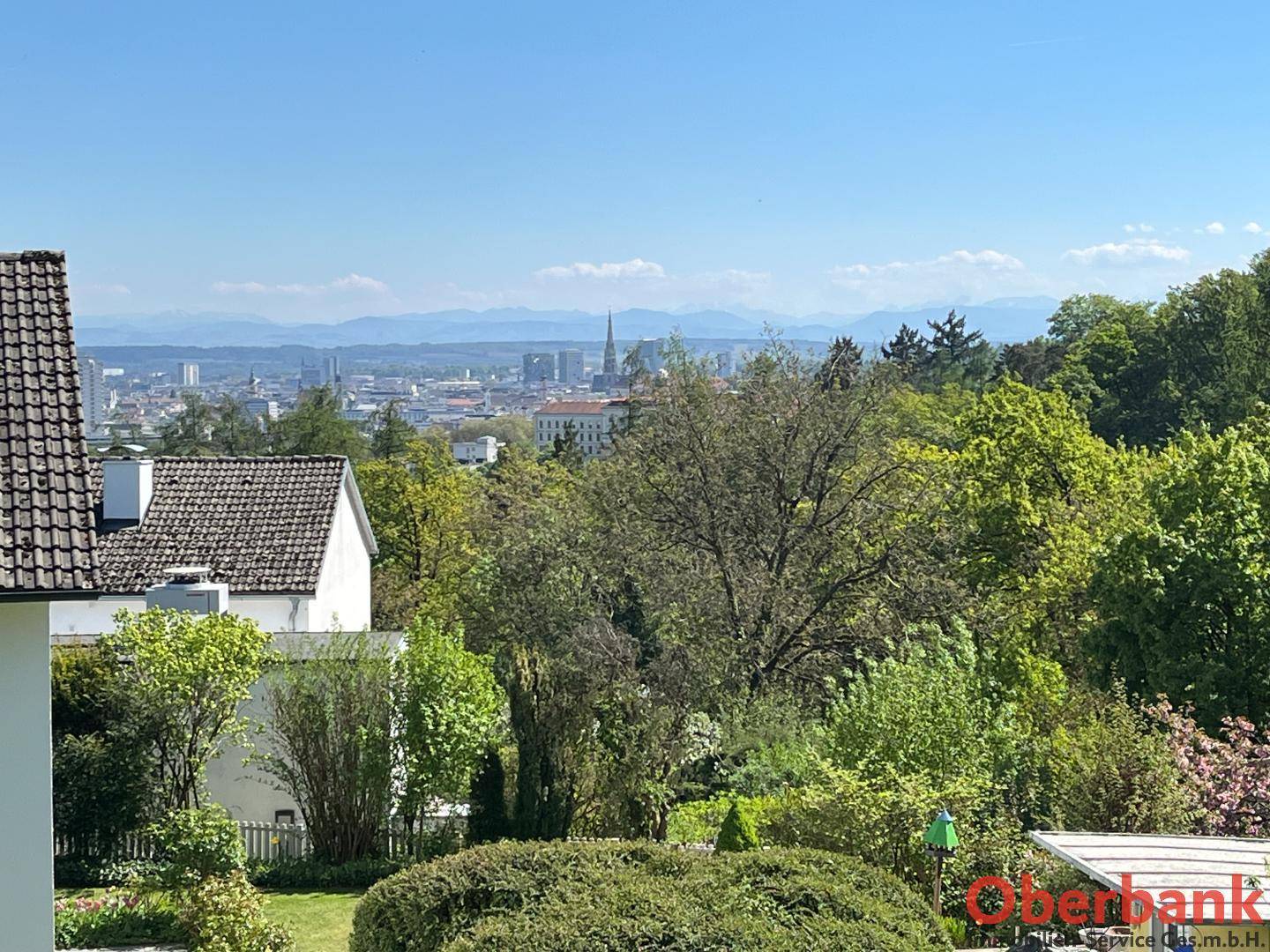 Weitläufiger Blick über die Stadt und die umliegende grüne Landschaft bis zu den fernen Bergen.