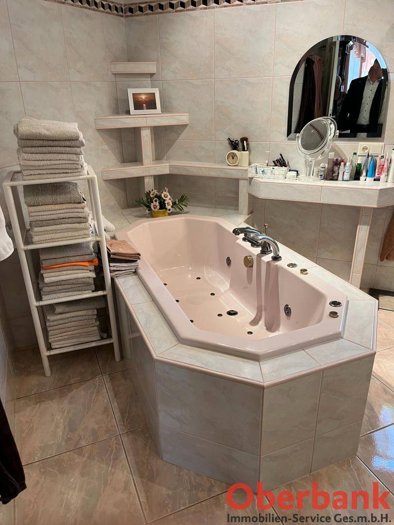 Badezimmer mit rosa Eckbadewanne, hellen Fliesen und Spiegelschrank.