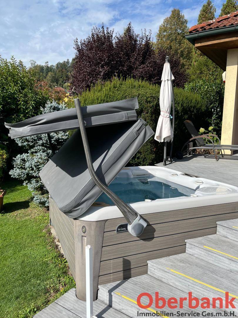 Entspannender Whirlpool auf der Holzterrasse, umgeben von üppigem Grün und Sonnenschirm.
