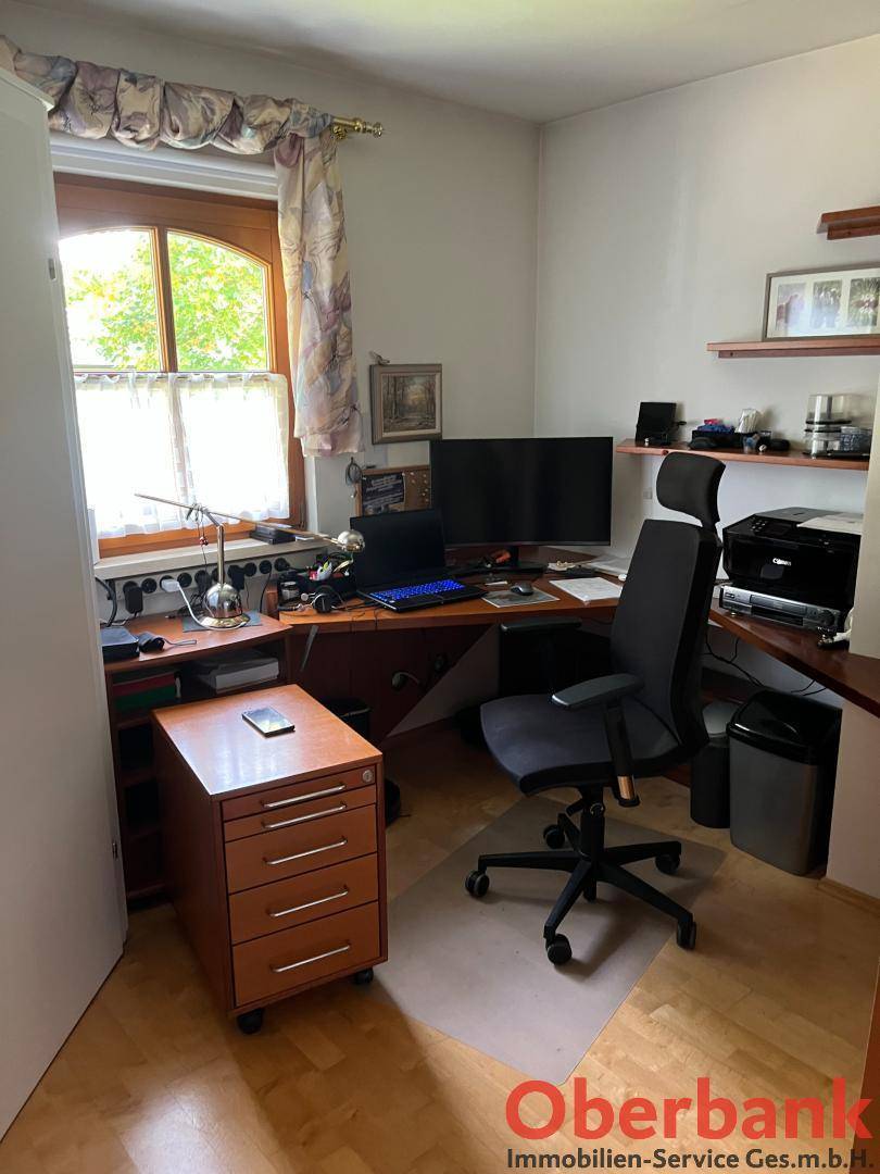 Funktionales Arbeitszimmer mit Holzschreibtisch, Bürostuhl und Fenster mit Blick ins Grüne.