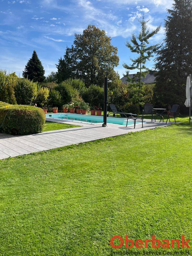 Großer, gepflegter Garten mit Rasenfläche, Pool und Liegestühlen unter strahlend blauem Himmel.