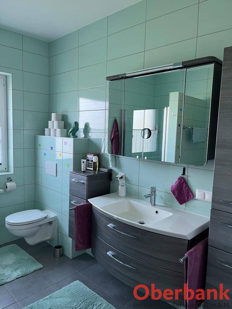 Modernes Badezimmer mit mintgrünen Fliesen, Waschtisch und Spiegelschrank.