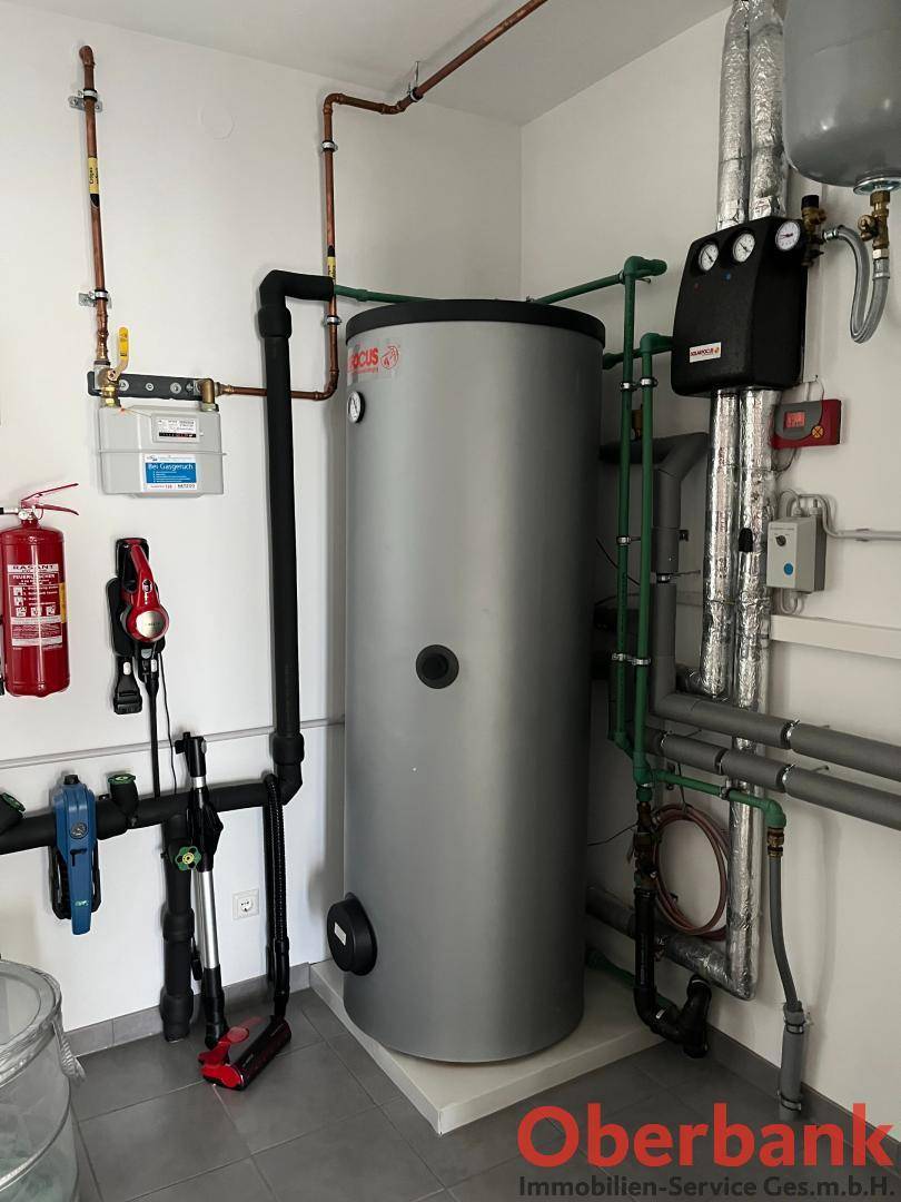 Technikraum mit Warmwasserspeicher, Heizungsanlage und sichtbaren Leitungen.
