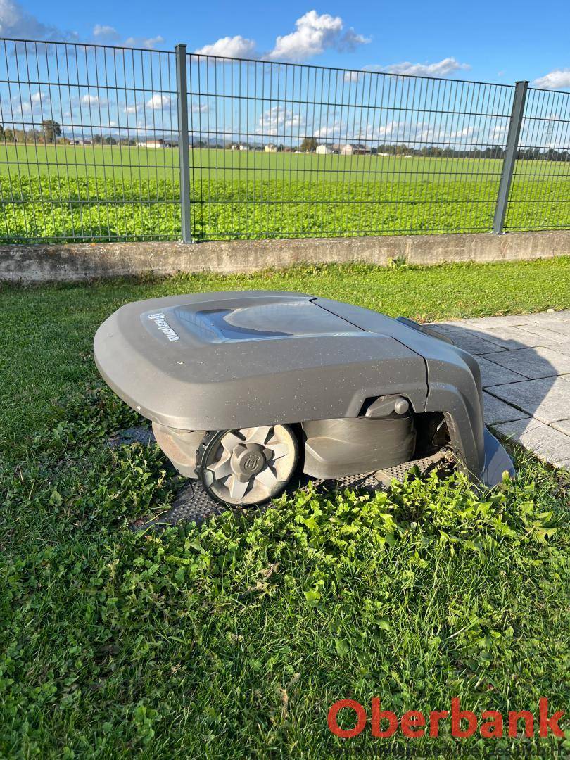 Roboter-Rasenmäher im Gartenbereich mit Blick auf grüne Felder.