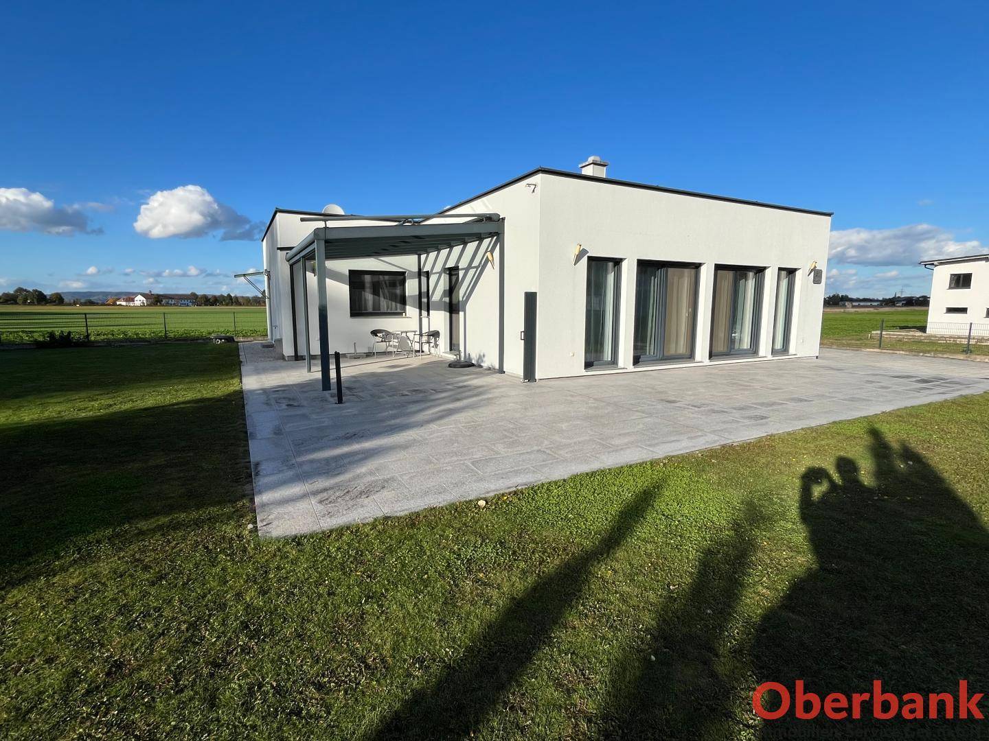 Rückseite des modernen Hauses mit großer gepflasterter Terrasse und weitem Blick ins Grüne.