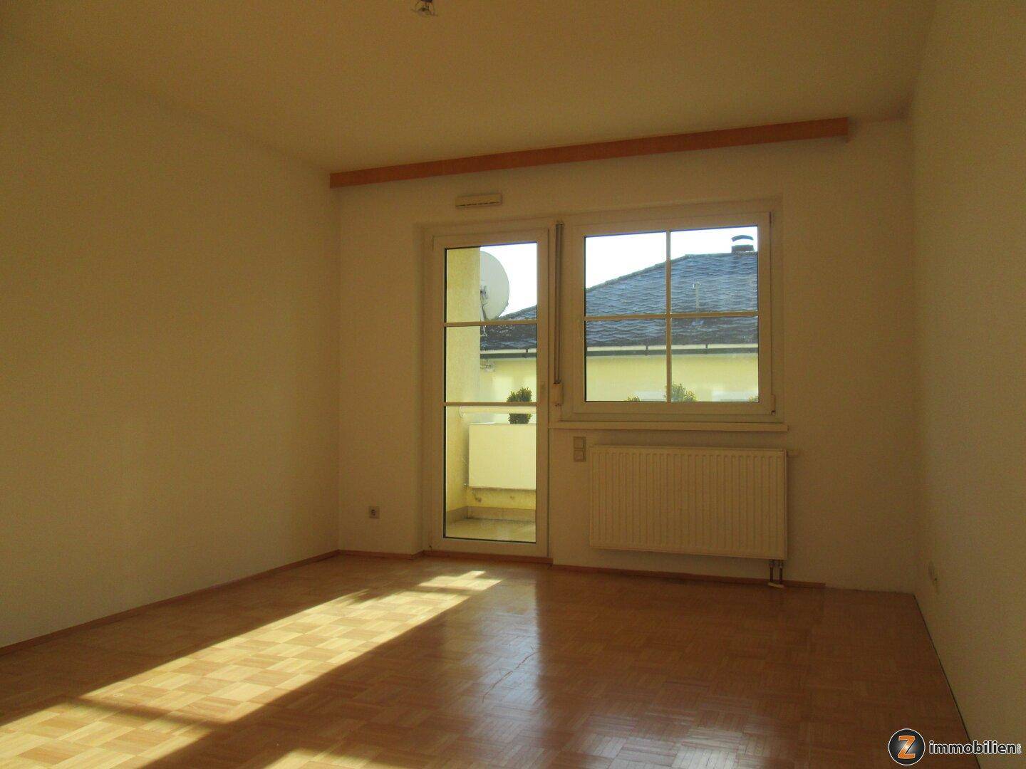 Heller Raum mit Parkettboden und Zugang zu einem kleinen Balkon.