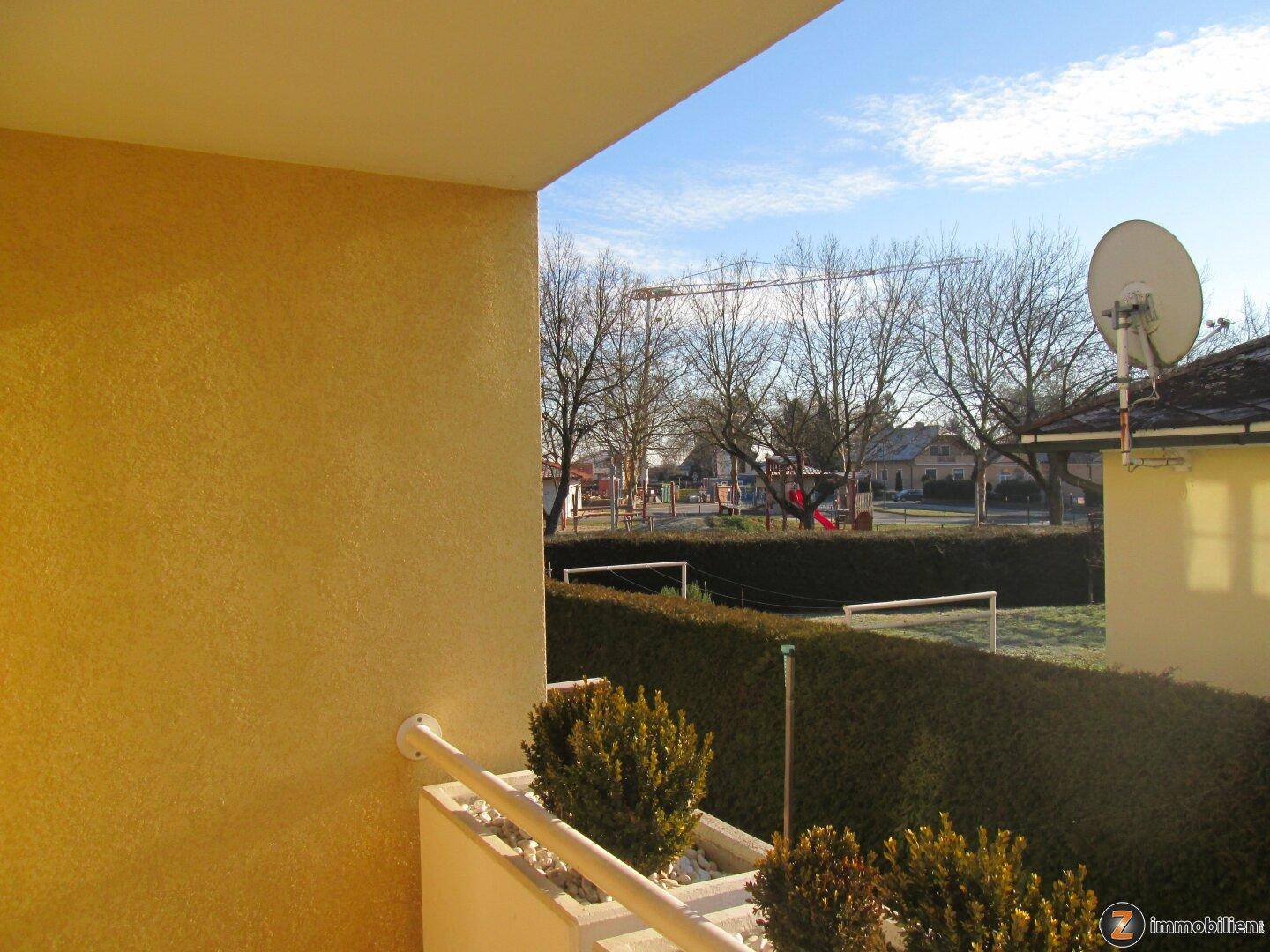 Balkon mit Blick auf einen Spielplatz und umliegende Bäume.