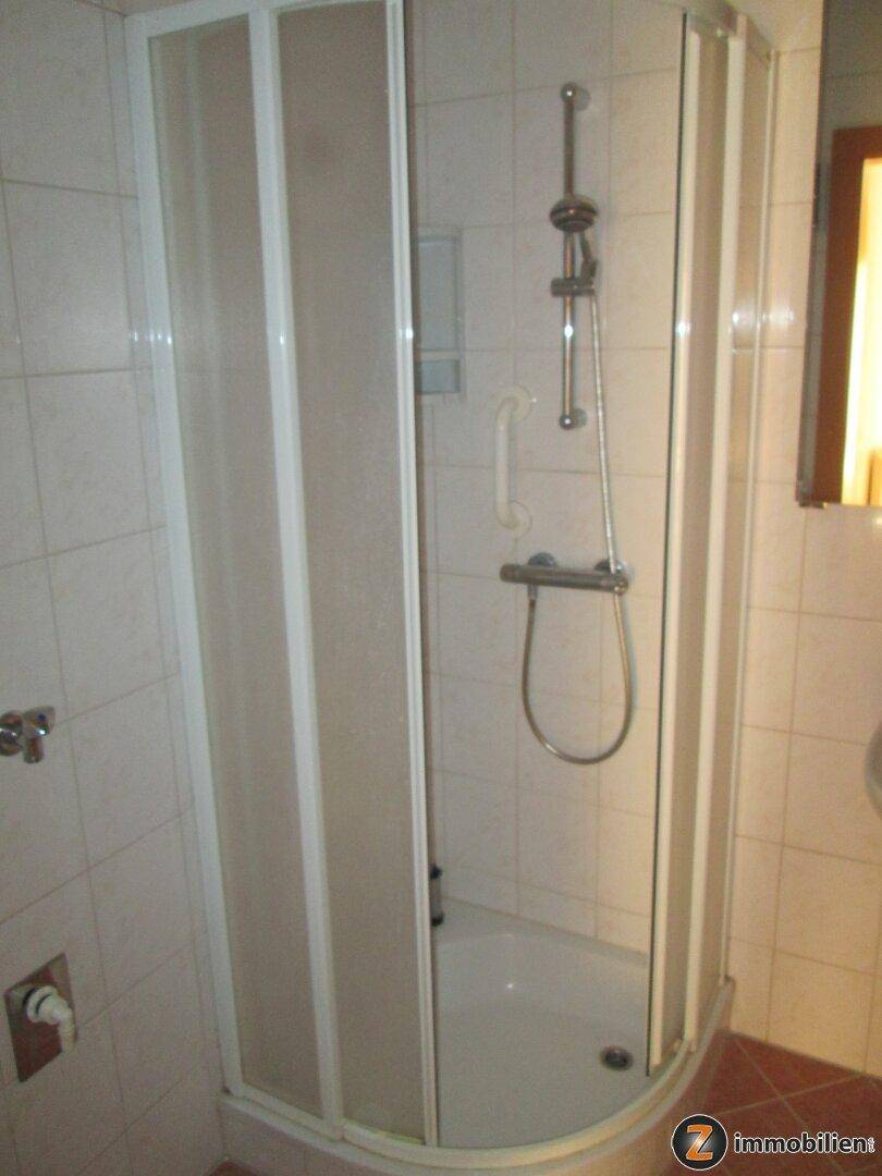 Badezimmer mit Eckdusche und hellen Fliesen an Wänden und Boden.