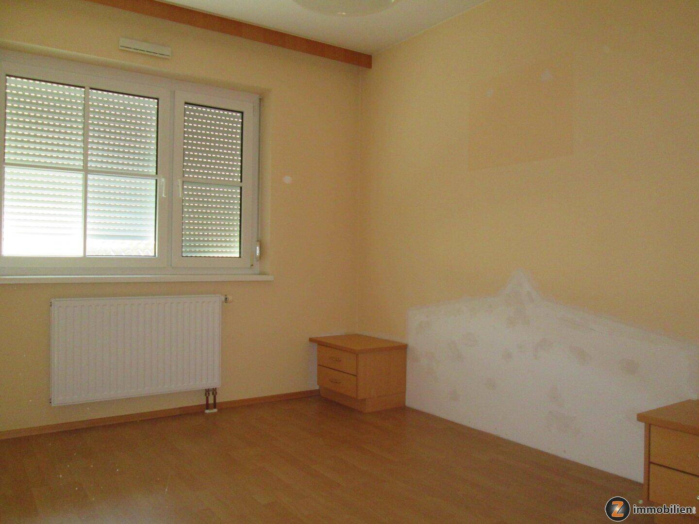 Schlafzimmer mit Laminatboden, Fenster mit Rollladen und zwei Nachttischen.