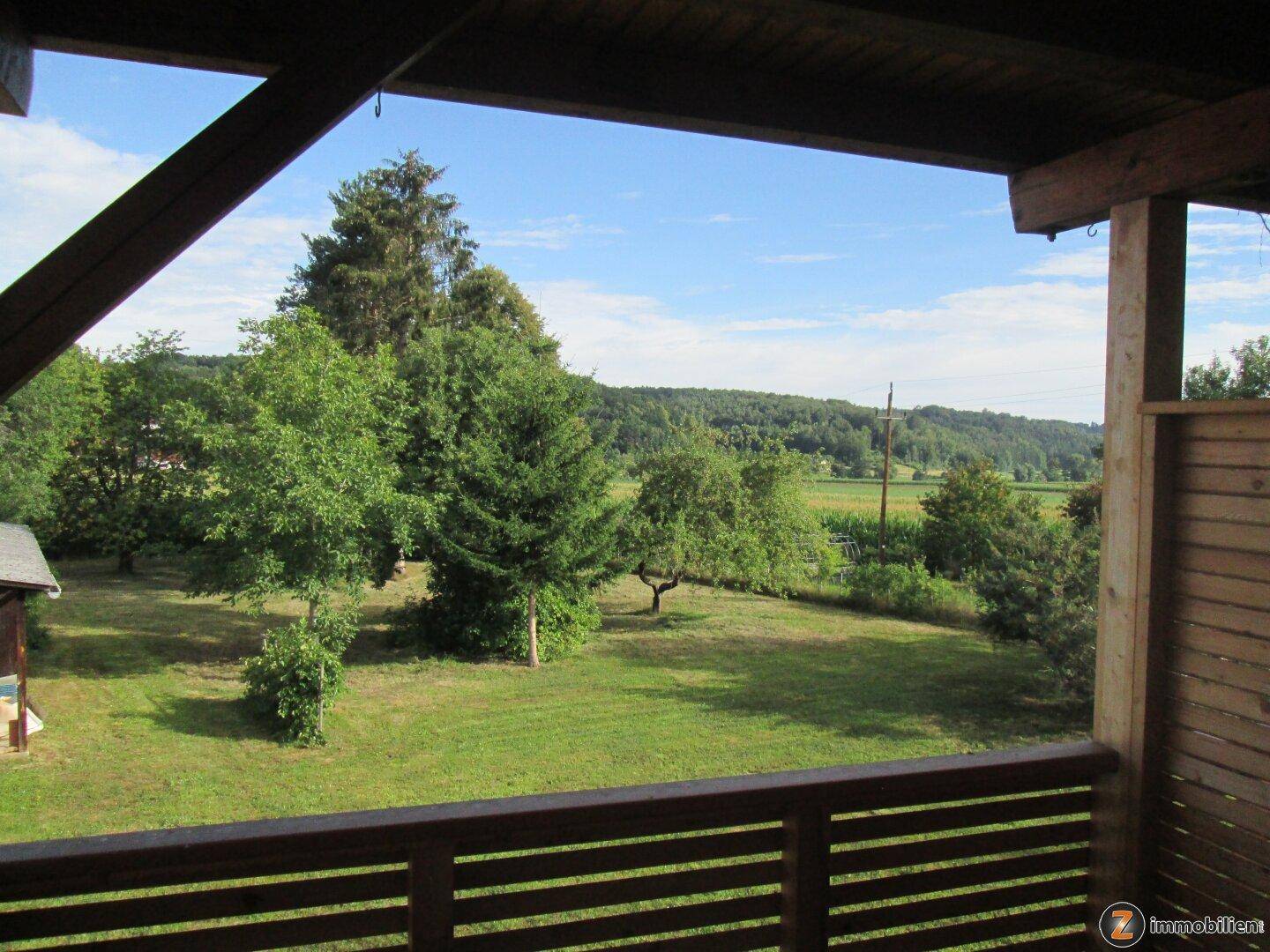 Balkon mit weitem Blick über grüne Felder und bewaldete Hügel in ländlicher Umgebung.