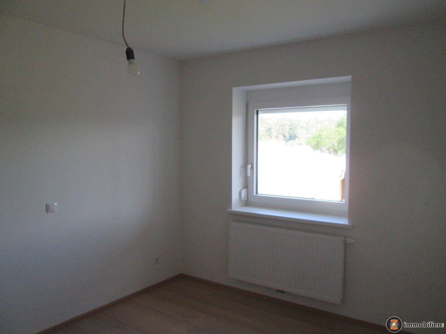 Heller, leerer Raum mit einem Fenster, Heizkörper und Holzboden.