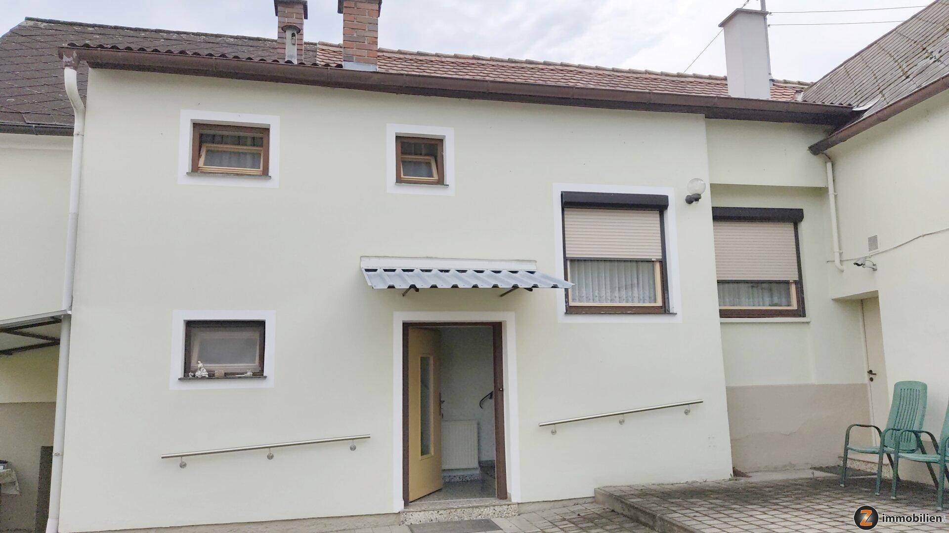 Eingangsbereich eines Gebäudes mit Rampe, Handläufen und Rollläden an den Fenstern.