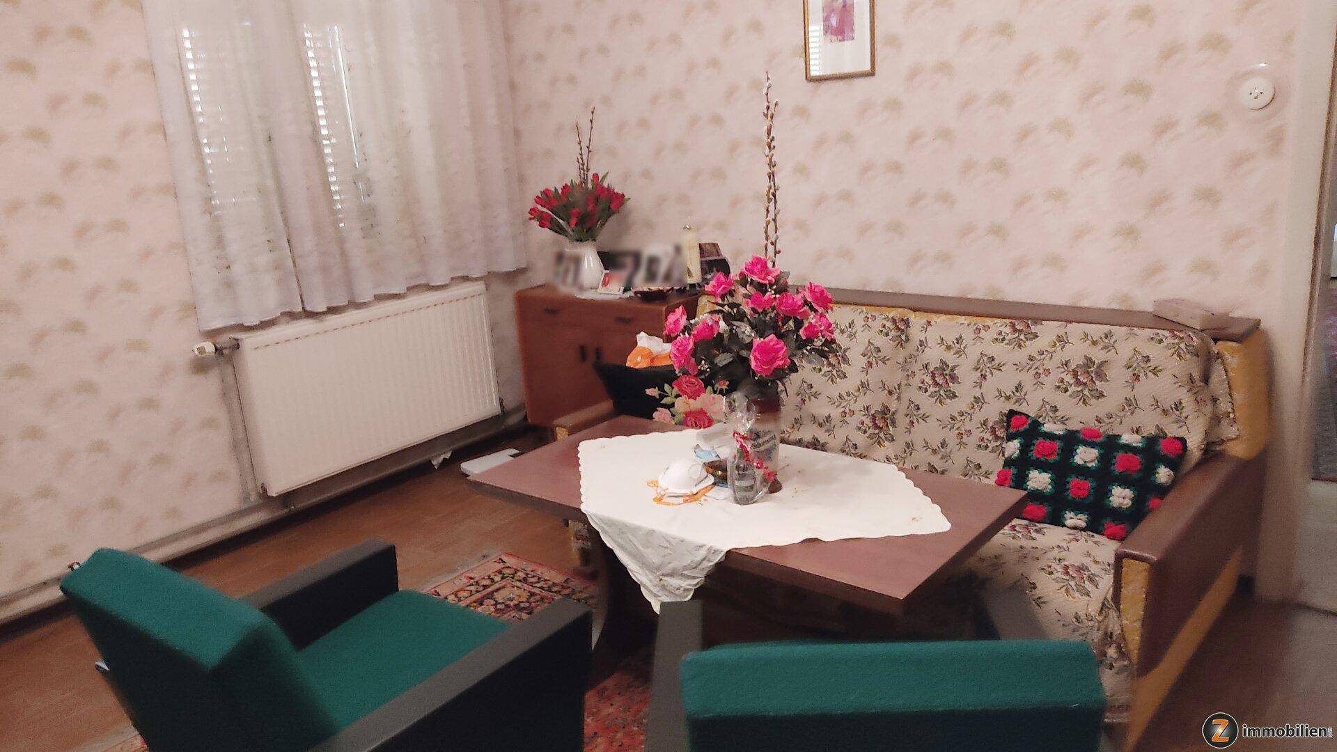 Gemütliches Wohnzimmer mit floraler Tapete, Sofa und einem Couchtisch mit Blumen.