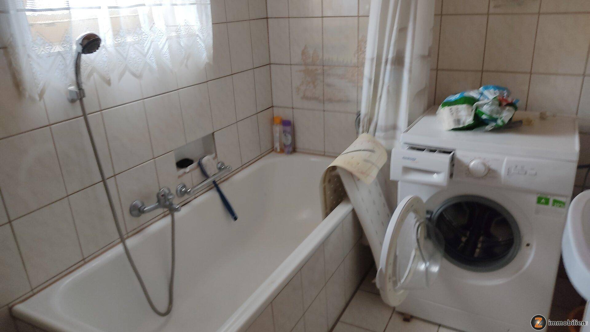 Badezimmer mit Badewanne, Fliesen an den Wänden und einer Waschmaschine.
