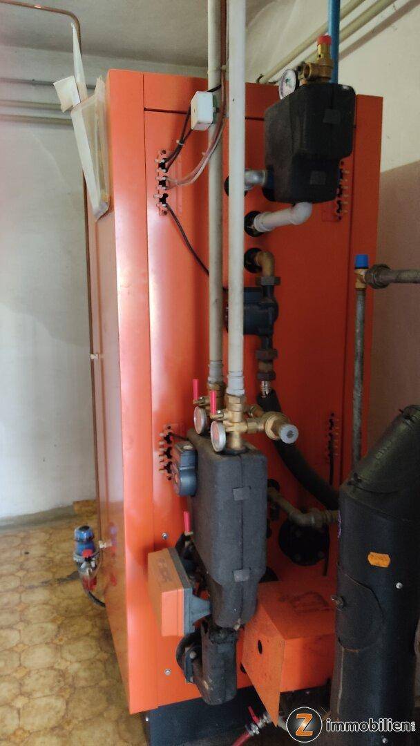 Heizungsraum mit einem großen orangefarbenen Heizkessel und sichtbaren Rohren.