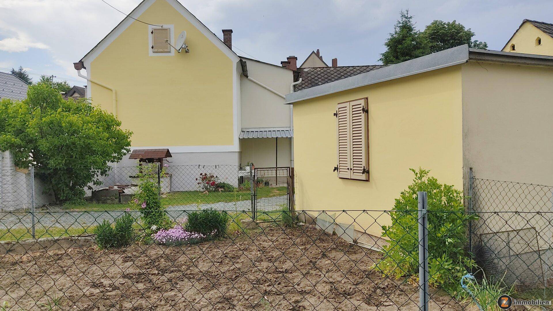 Rückseite des Hauses und Nebengebäude mit einem kleinen Gartenbereich und Zaun.