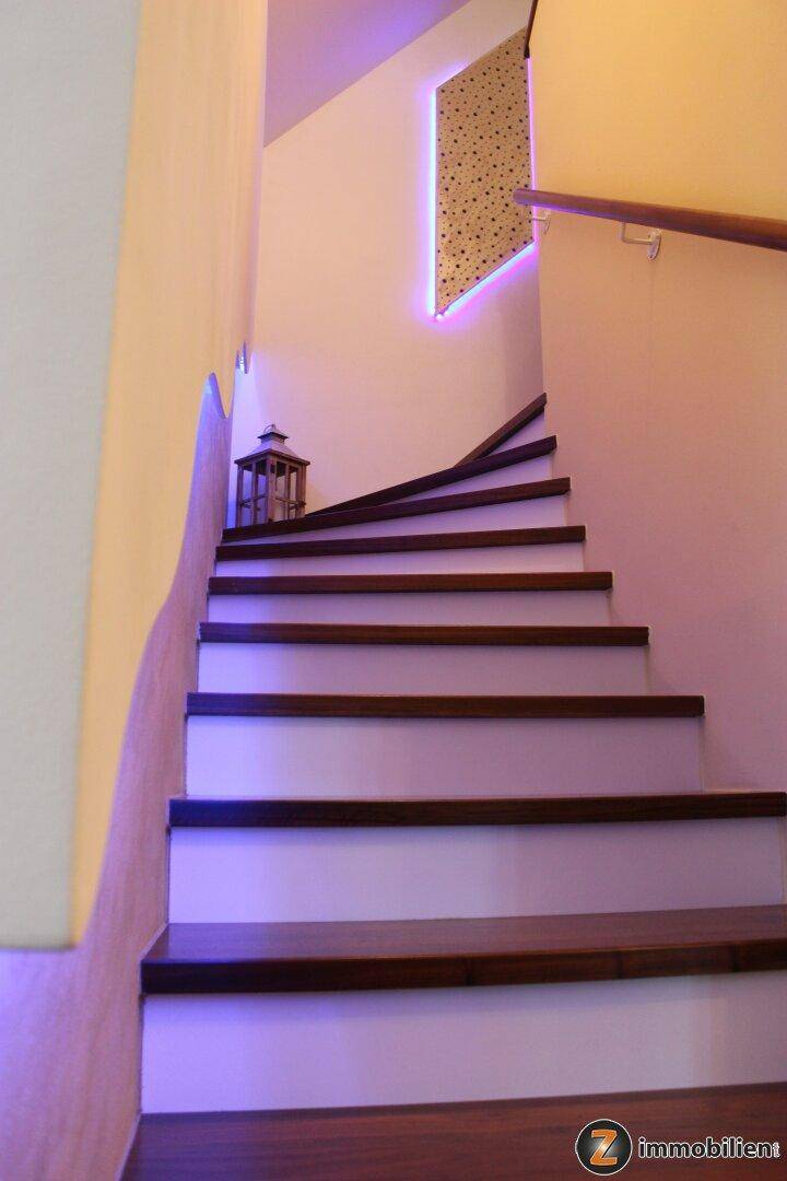 Moderner Treppenaufgang mit Holzstufen, indirekter Beleuchtung und minimalistischer Dekoration.
