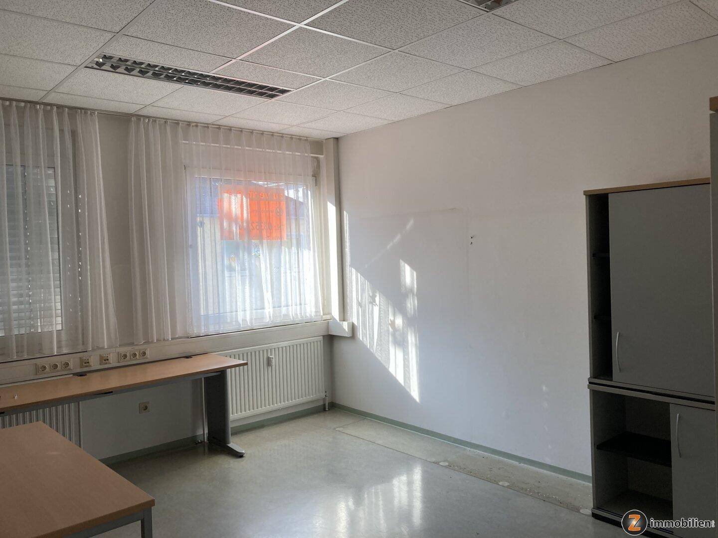 Büro mit zwei Fenstern, Heizkörpern und einem Schreibtisch, bietet viel Tageslicht für eine angenehme Arbeitsatmosphäre.