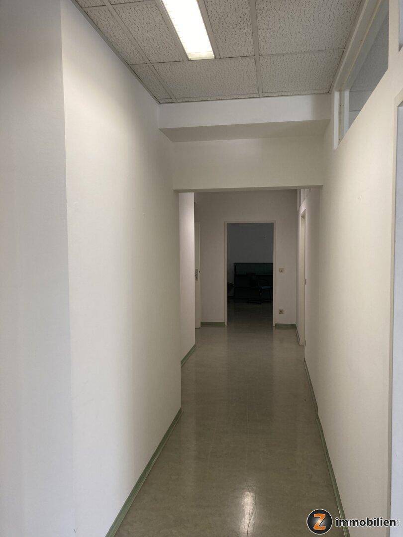 Heller Flur mit weißen Wänden und einem glänzenden Boden, der zu weiteren Räumen führt.